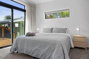 a white bedroom with a bed and a large window at Recline on Leo in Waihi Beach