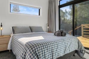a bedroom with a bed with a checked blanket and a window at Recline on Leo in Waihi Beach