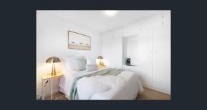 a white bedroom with a bed and a table with a lamp at Seaside Adelaide Holiday Apartment 2BR 1 min walk to Brighton Beach in Adelaide