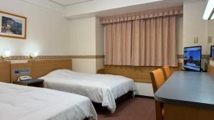 a hotel room with two beds and a desk at Hotel Alpha-One Hofu in Hofu