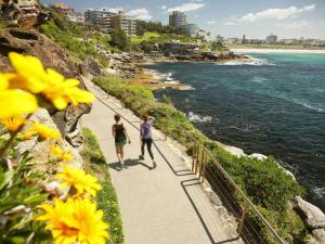 two people walking down a sidewalk next to the ocean at Cozy Bondi Apartment Heated Winter Stay in Sydney