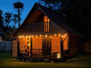 a woman sitting on a couch in front of a cabin with lights at Zacisze nad Jeziorem- prywatny domek blisko morza in Jezierzany
