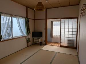 a living room with a television and two windows at ゲストハウス凪季のやど in Nachikatsuura