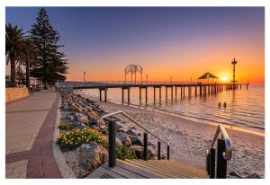 a pier on the beach with the sun setting at Seaside Adelaide Holiday Apartment 2BR 1 min walk to Brighton Beach in Adelaide