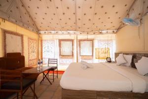 a bedroom with a bed and a table and windows at Rumis Desert Camp in Jaisalmer