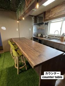 a kitchen with a wooden table and some green chairs at ゲストハウスこだまのおうち in Asahikawa