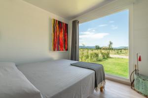 a bedroom with a bed and a large window at Macondo Agriliving Tiny Houses in Castiadas