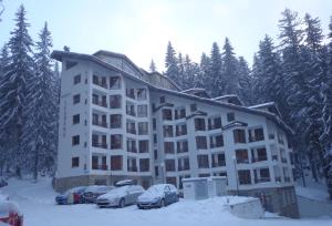 duży budynek apartamentowy z samochodami zaparkowanymi na śniegu w obiekcie Ski & Holiday Apartments in Pamporovo w mieście Pamporowo