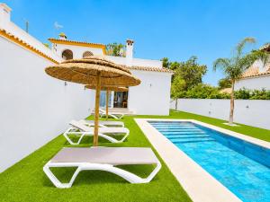 a villa with a swimming pool with two chairs and an umbrella at Playa Fuente del Gallo I in Conil de la Frontera +25 photos