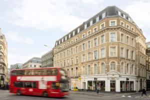 a red double decker bus driving past a building at COVE Cannon Street in London