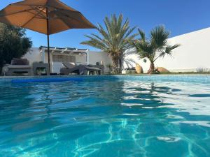 a swimming pool with an umbrella and palm trees at Villa Dar La Belle Beyah - Tezdaine in Taguermess