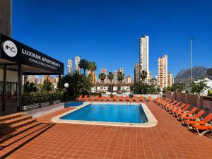 a swimming pool with orange chairs and a city at Luxmar Apartaments By MC in Benidorm