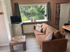 a living room with a brown couch and a window at Bungalow Halfweg in Ballum