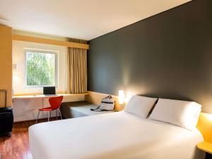 a bedroom with a white bed and a desk and a window at Ibis Monterrey Valle in Monterrey