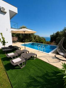 a swimming pool with chairs and an umbrella next to a yard at Villa Deromano in Šušanj