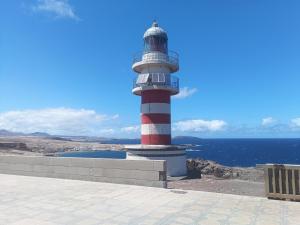 a red and white lighthouse on the side of the ocean at Alojamiento Gofioplaya in Arinaga