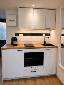 a kitchen with white cabinets and a black appliance at Kajüte mit Meerblick & eigener Terrasse in Sierksdorf