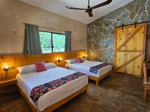 a bedroom with two beds and a stone wall at Cabañas Chechén Chaká in Leona Vicario