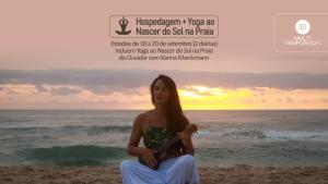 a woman sitting on the beach playing a guitar at Villa Verde Bangalô - Garopaba - SC in Garopaba
