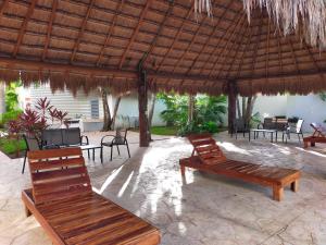a patio with chairs and a straw umbrella and benches at CasaMEXH Lunamar - Despierta, toma café en la 5ta Av, explora Xcaret, experimenta Tulum o algún cenote cercano - Unas vacaciones extraordinarias para tu familia y tus amigos in Playa del Carmen