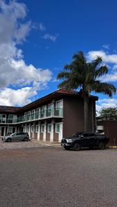 a black limo parked in front of a building with a palm tree at Hotel Ponto 1 in Vacaria