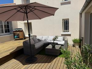 a patio with a couch and an umbrella at Le havre des embruns in Saint-Xandre