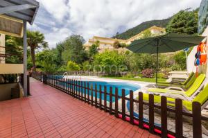 a pool with chairs and an umbrella next to a house at Casa da Lagoa II in Terras de Bouro