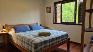 a bedroom with a bed with blue pillows and a window at Surf a poucos passos do mar, casa com lareira in Garopaba