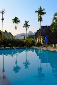 a blue swimming pool with palm trees in the background at Romantic Vang Vieng resort in Vang Vieng