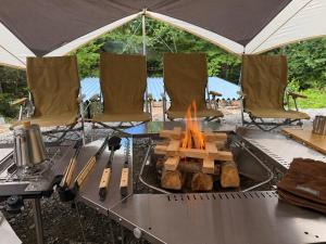 a grill with a fire on a table with chairs at 1日1組様限定 最大10名様 キャンプ 温泉付き Villa 水と深緑 in Azumino