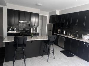 a kitchen with black cabinets and two bar stools at Gifted Beautiful Home in Brampton +17 photos