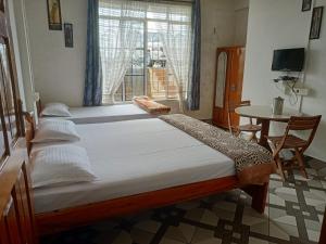 a bedroom with two beds and a table and a window at Vibgyor Hotel in Cherrapunji