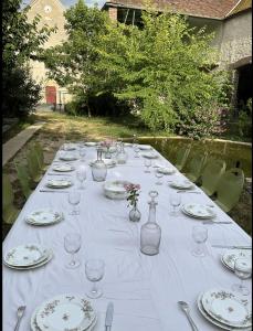 a long white table with plates and glasses on it at Grand corps de ferme à la rue Messire Etienne 89113 Neuilly Valravillon in Neuilly