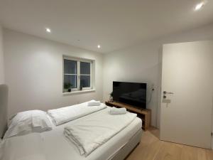a white bedroom with a bed and a flat screen tv at Living by Maier Altach in Altach