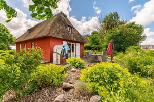 a red house with a thatched roof in a garden at Ferienhaus Hyggehüs in Risum-Lindholm