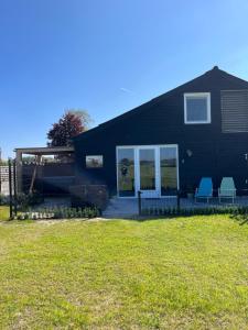 a black house with two blue chairs in the yard at B&B de Landstreek in Hulten