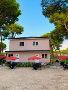 a building with tables and red umbrellas in front of it at Vila Topi in Vlorë