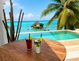two cocktails sitting on a wooden table next to a pool at Villa Duara Zanzibar Rooftop Infinity Pool The Rock View in Michamvi