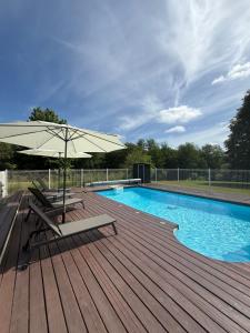 a wooden deck with an umbrella next to a swimming pool at Les gîtes de la Joubertie in Salon