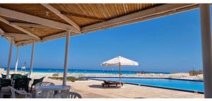 a patio with a table and an umbrella next to the beach at فيلا بسين خاص in Dawwār Abū Maḩrūs