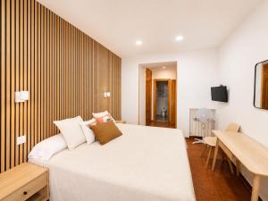 a bedroom with a large white bed and a desk at Hostal Bellas in Ávila
