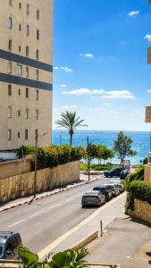 a street with cars parked next to a building and the ocean at Royal Lea Apartmens in Netanya