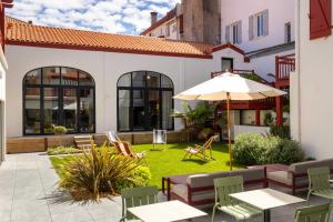 an outdoor patio with tables and chairs and an umbrella at Hôtel Kemaris in Biarritz