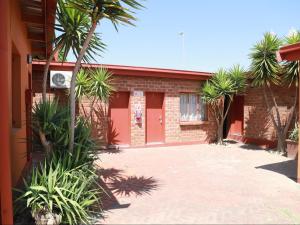 a red brick building with palm trees in front of it at Oluzizi Guesthouse in Windhoek