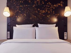 a bed with white pillows and two lights on it at Mercure Paris La Défense in Courbevoie