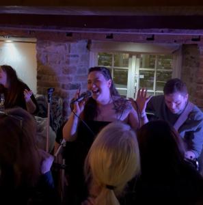 a woman singing into a microphone at a party at The Manor House Hotel in Dronfield