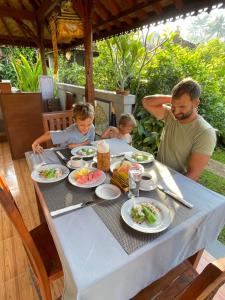 a man and two children sitting at a table with food at Pondok Indah Homestay in Sidemen
