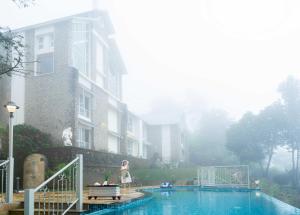 a woman walking by a swimming pool in front of a house at 1924 Clock House Munnar in Munnar