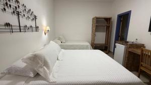 a white bedroom with two beds and a mirror at Pousada Pouso de Laura in Tiradentes