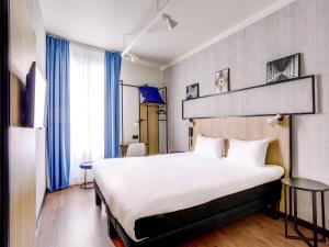 a hotel room with a large white bed and blue curtains at ibis Daumesnil Porte Doree in Paris